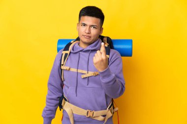 Sarı arka planda izole edilmiş büyük sırt çantalı genç dağcı geliyor.