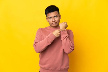 Genç Ekvadorlu adam sarı arka planda izole edilmiş, geç kalma jesti yapıyor.