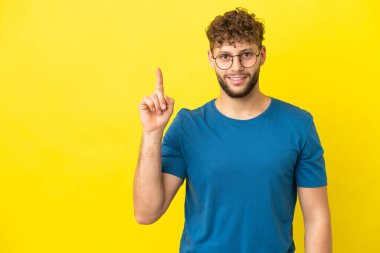Sarı arka planda izole edilmiş yakışıklı beyaz adam harika bir fikre işaret ediyor.