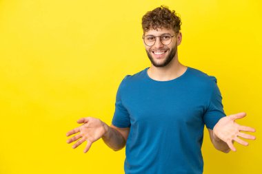 Sarı arka planda izole edilmiş yakışıklı beyaz adam mutlu ve gülümsüyor.