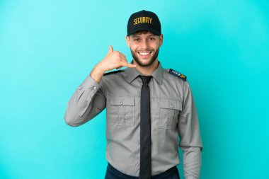 Genç güvenlik görevlisi mavi arka planda izole edilmiş bir şekilde telefon jesti yapıyor. Bana geri dönüş işareti ver.