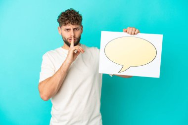 Genç, beyaz, mavi arka planda izole edilmiş genç bir adam elinde konuşma baloncuğu ikonlu bir pankartla sessizlik hareketi yapıyor.