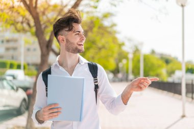 Dışarıdaki yakışıklı öğrenci bir ürün sunmak için yan tarafı işaret ediyor.