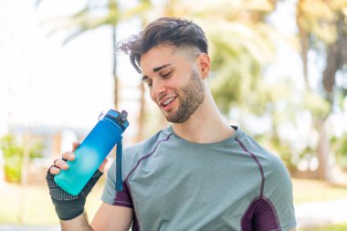 Genç yakışıklı bir adam bir şişe suyla spor yapıyor.
