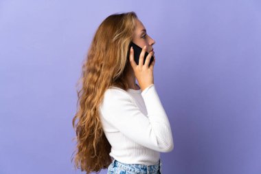 Mor arka planda izole edilmiş genç sarışın bir kadın cep telefonuyla sohbet ediyor.