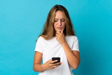 Genç sarışın kadın mavi arka planda izole edilmiş düşünüyor ve bir mesaj gönderiyor.