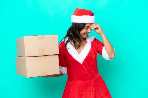 Young hispanic woman dressed as mama noel holding cartoon box isolated on blue background laughing