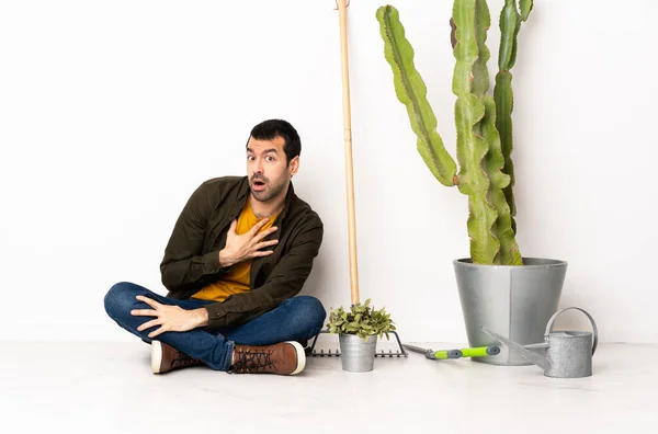 Gardener man sitting on the floor at indoors surprised and shocked while looking right