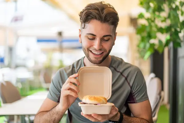 Young handsome man holding a burger with happy expression