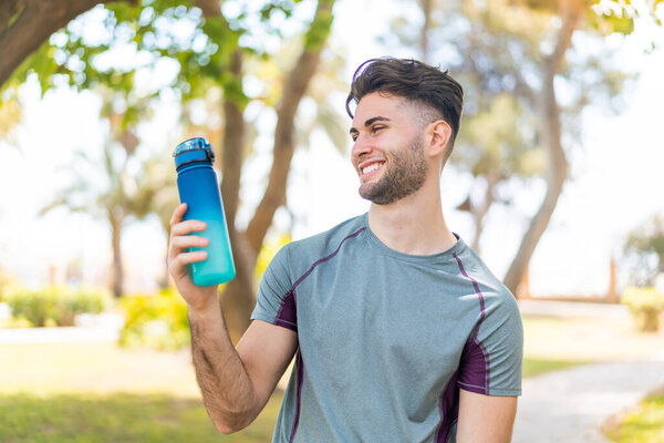 Young handsome sport man with a bottle of water at outdoors with happy expression
