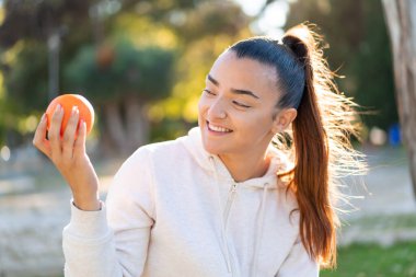 Genç, güzel esmer kadın elinde portakalla dışarıda mutlu bir ifadeyle bekliyor.