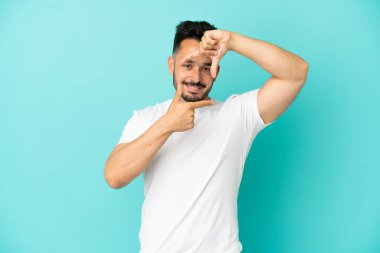 Young caucasian man isolated on blue background focusing face. Framing symbol