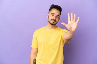 Mor arka planda izole edilmiş genç beyaz adam parmaklarıyla beşi sayıyor.