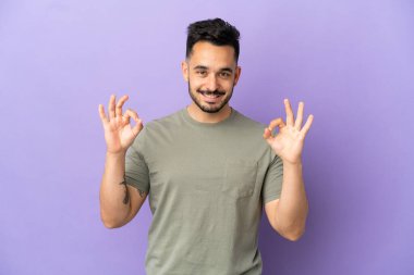 Mor arka planda izole edilmiş beyaz bir adam iki eliyle tamam işareti gösteriyor.