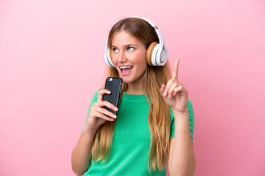 Pembe arka planda izole edilmiş genç sarışın bir kadın cep telefonuyla müzik dinliyor ve şarkı söylüyor.