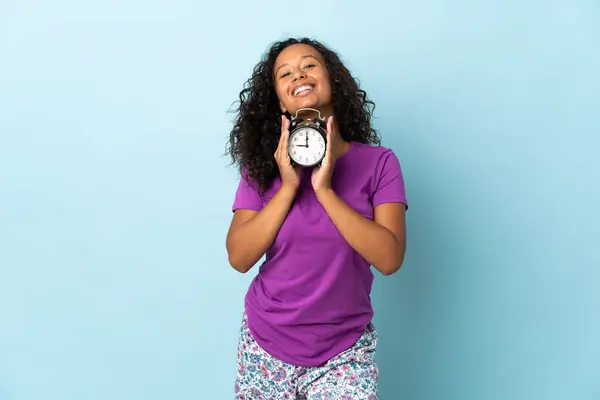 Teenager Cuban Girl Isolated Blue Background Pajamas Holding Clock Happy — Stock Photo, Image