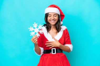 Anne Noel gibi giyinmiş, mavi arka planda izole edilmiş bir kar tanesi tutan genç İspanyol kadın. Çok gülümsüyor.