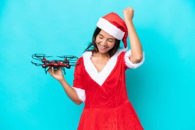 Anne Noel gibi giyinmiş genç bir kadın mavi arka planda izole edilmiş bir drone tutuyor ve zaferi kutluyor.