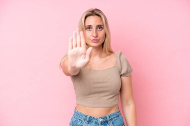 Pembe arka planda izole edilmiş genç beyaz kadın dur hareketi yapıyor.