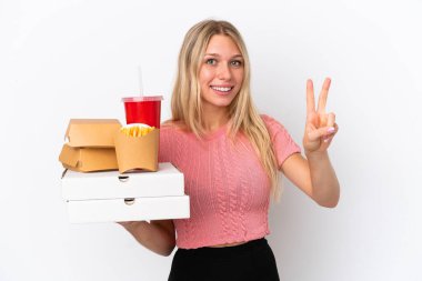 Mavi arka planda yağlı yiyecekler taşıyan beyaz kadın gülümsüyor ve zafer işareti gösteriyor.