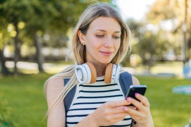 Açık havada cep telefonu kullanan genç sarışın kadın.