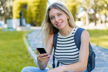 Açık havada cep telefonu kullanan genç sarışın kadın.