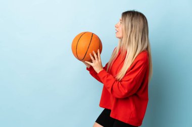 Genç sarışın kadın mavi arka planda izole edilmiş basketbol oynuyor.