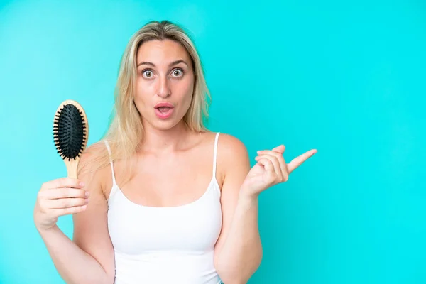Young Caucasian Woman Hair Comb Isolated Blue Background Surprised Pointing —  Fotos de Stock