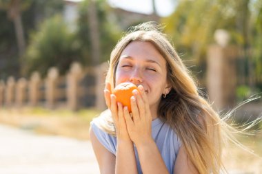 Açık havada elinde portakal tutan genç sarışın kadın.