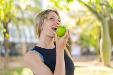 Açık havada, elinde elma tutan genç sarışın kadın.