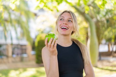 Açık havada elinde mutlu bir ifadeyle bir elma tutan genç sarışın kadın.