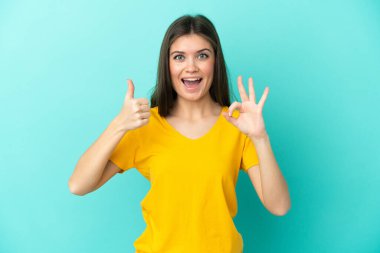 Mavi arka planda izole edilmiş genç beyaz kadın işaret ve baş parmak hareketi gösteriyor.
