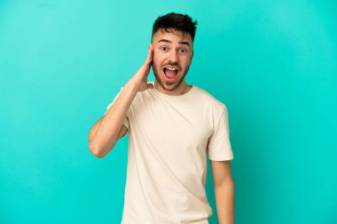 Mavi arka planda mahsur kalmış, şaşırmış ve şok olmuş genç bir beyaz adam.