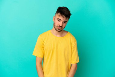 Hüzünlü bir ifadeyle mavi arka planda izole edilmiş genç beyaz bir adam.