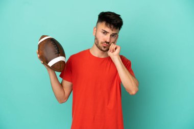 Genç beyaz adam rugby oynuyor. Mavi arka planda izole edilmiş bir şekilde bir fikir düşünüyor.
