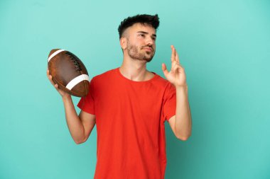 Genç beyaz adam rugby oynuyor. Mavi arka planda izole edilmiş, şans diliyor ve en iyisini diliyor.