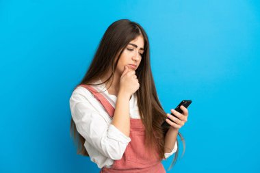 Genç beyaz kadın mavi arka planda izole edilmiş düşünüyor ve bir mesaj gönderiyor.