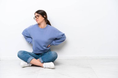 Beyaz arka planda izole bir şekilde yerde oturan beyaz bir kadın çaba gösterdiği için sırt ağrısından muzdarip.