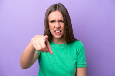Mor arka planda izole edilmiş genç beyaz kadın hayal kırıklığına uğramış ve ön tarafı işaret ediyor.