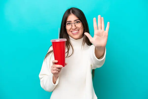 Young caucasian woman drinking soda isolated on blue background counting five with fingers