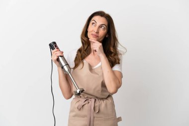 Beyaz arka planda izole edilmiş el blenderi kullanan orta yaşlı beyaz bir kadın.