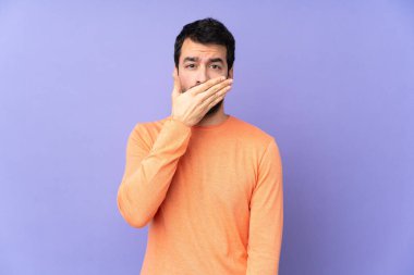 İzole edilmiş mor arka planı olan beyaz, yakışıklı bir adam elleriyle ağzını kapatıyor.