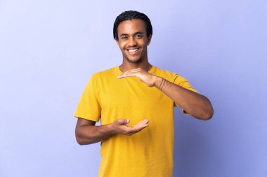 Örgülü genç Afrikalı Amerikalı adam, mor arka planda izole edilmiş. Kopya uzay hayali bir ilan vermek için avucunun içinde duruyor.