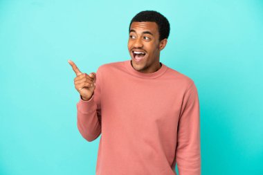 İzole edilmiş mavi arka plandaki Afro-Amerikalı yakışıklı adam parmağını kaldırarak çözümü bulmaya çalışıyor.