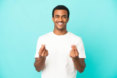 İzole edilmiş mavi arka planda Afro-Amerikalı yakışıklı adam para hareketi yapıyor.