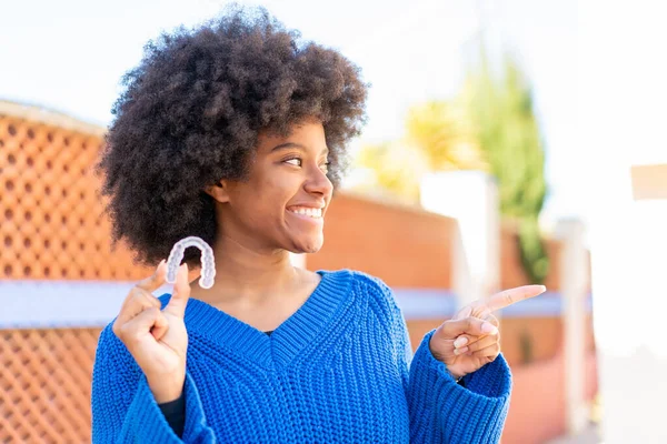African American Girl Holding Invisible Braces Outdoors Pointing Side Present — Stock Photo, Image