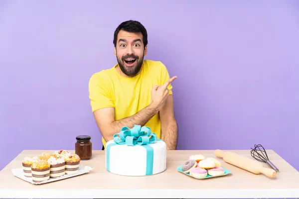 Man in a table with a big cake surprised and pointing side