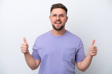 Beyaz arka planda izole edilmiş genç beyaz bir adam baş parmak hareketi yapıyor.