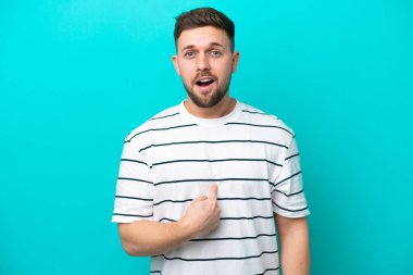 Mavi arka planda izole edilmiş genç beyaz adam kendini işaret ediyor.