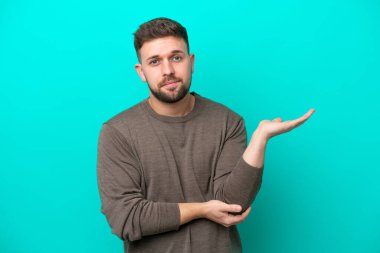 Kafkasyalı genç adam mavi arka planda izole edilmiş. Şüpheleri var.